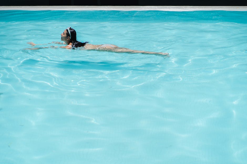 A person swimming laps in a pool with a smile on their face. The water is crystal clear and the sun is shining brightly, indicating a beautiful day.